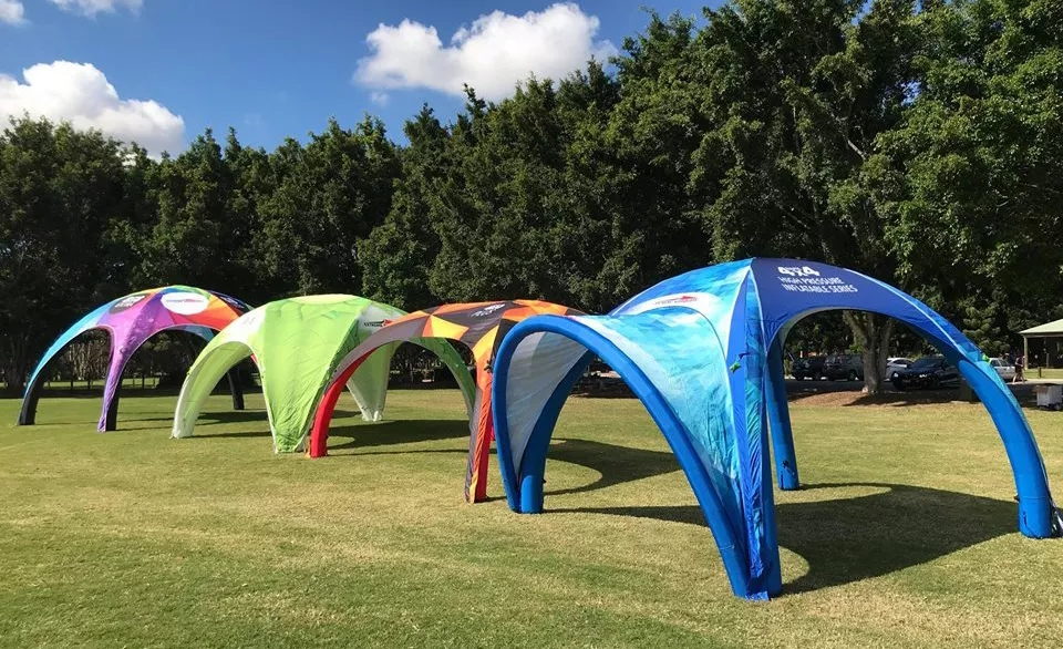 Row of printed arc tents with curved aluminium frames set up on a lawn at an outdoor event